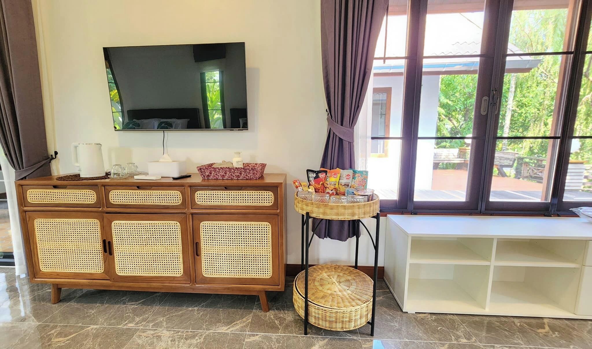 Una habitación con un armario de madera con puertas tejidas, un televisor encima, una cesta de mimbre y un banco blanco.