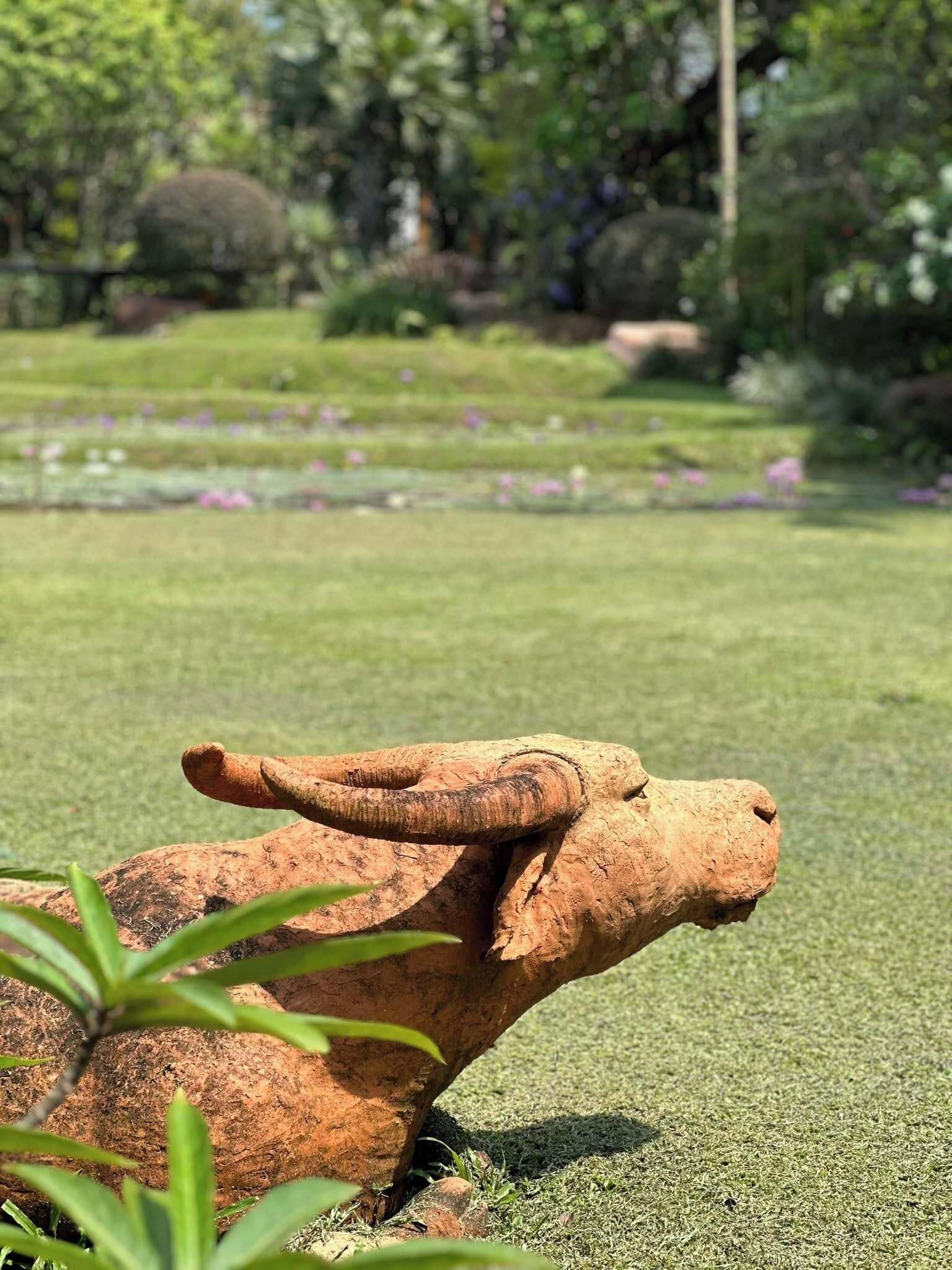 Une sculpture de buffle dans un jardin, avec de l’herbe et des fleurs.