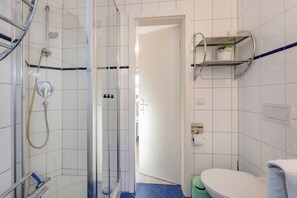 Ein Badezimmer mit einer Duschkabine, einer Toilette und einem Ablagefach für Pflegeprodukte.