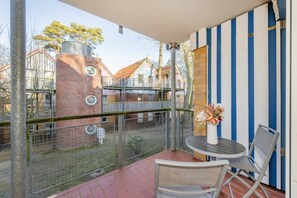 Ein Balkon mit Tisch, Stühlen, einer Blumenvase und Blick auf ein Backsteingebäude mit Schornstein.