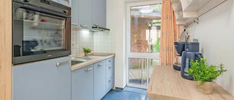 A compact kitchen with a built-in oven, a sink, and a coffee machine on a wooden countertop.