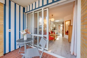 Ein Balkon mit Tisch und Stühlen, eine Glastür, die zu einem Innenraum mit Essbereich und Küche führt.