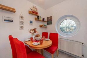 A dining area with a round table, red chairs, a window with a view, and various wall decorations. - Cozy vacation apartment in Koserow with sea view - only 50 m to the beach! - (Koserow)
