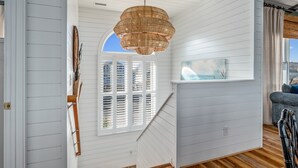 A staircase with white paneling, a wicker chandelier, and a view of the outdoors through a window with shutters. - "Paradise Palms" 3 Bedroom 3.5 Bath Second Row Home! (Supply)