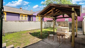A backyard with a wooden pergola, a white sofa, and a wicker chair.