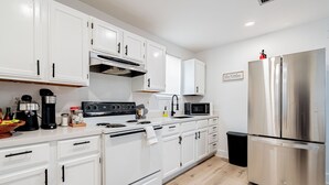 A modern kitchen with white cabinets, stainless steel appliances, and a black trash bin.