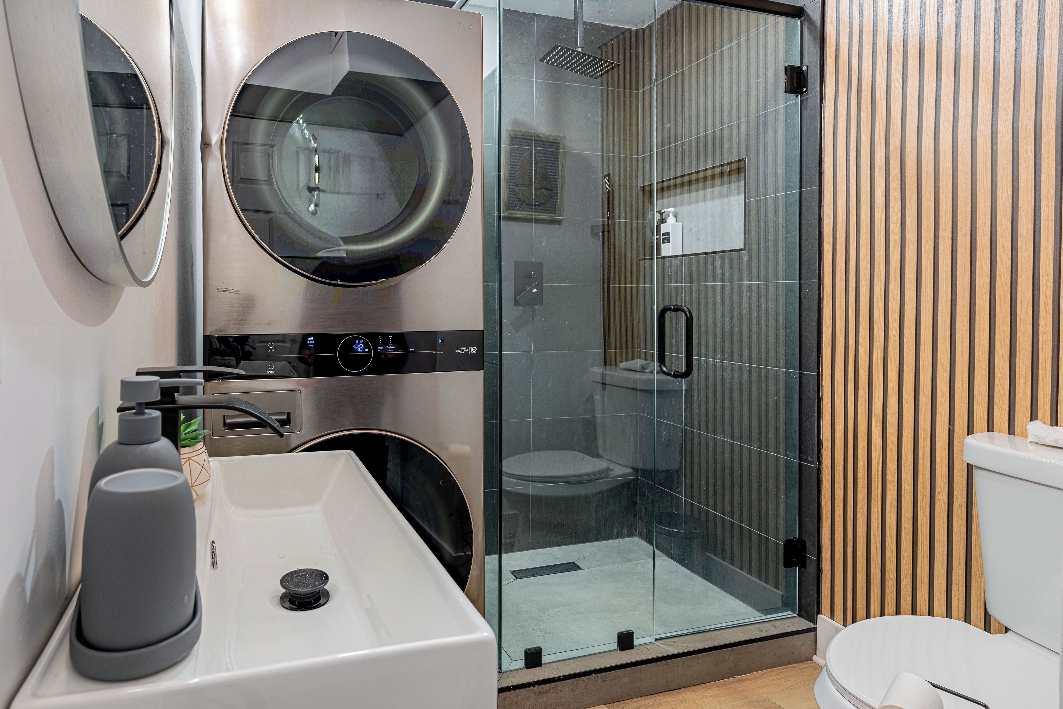 Ein modernes Badezimmer mit einer Duschkabine, einer integrierten Waschmaschine und einem Waschbecken mit Seifenspender.
