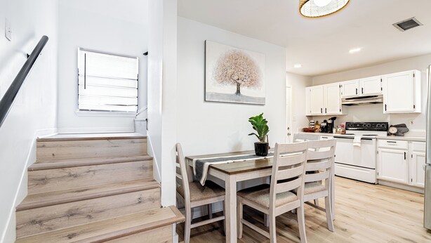A modern kitchen with white cabinets, a wooden dining table, and a staircase leading to another level.