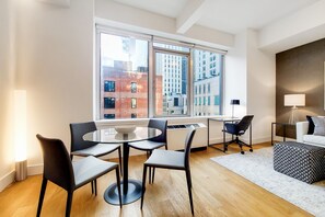A modern living room with a round glass table, black chairs, a white sofa, and a patterned ottoman. - Spacious Studio With Luxury Amenities | Tribeca (New York)