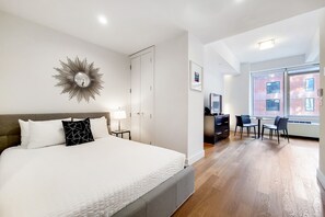 A hotel room with a large bed, a desk with a chair, a TV, and a window with a city view. - Spacious Studio With Luxury Amenities | Tribeca (New York)