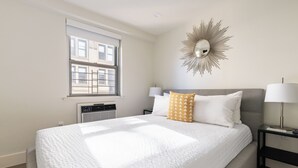 Hotellihuone, jossa on suuri sänky, kaksi yöpöytävalaisinta, seinälle kiinnitetty peili ja ikkuna, jossa on sälekaihtimet.