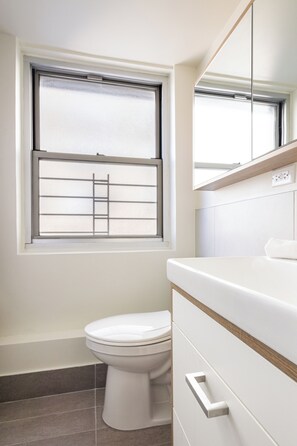 Un bagno con il water, una finestra con una griglia metallica e uno specchio sopra il lavandino.