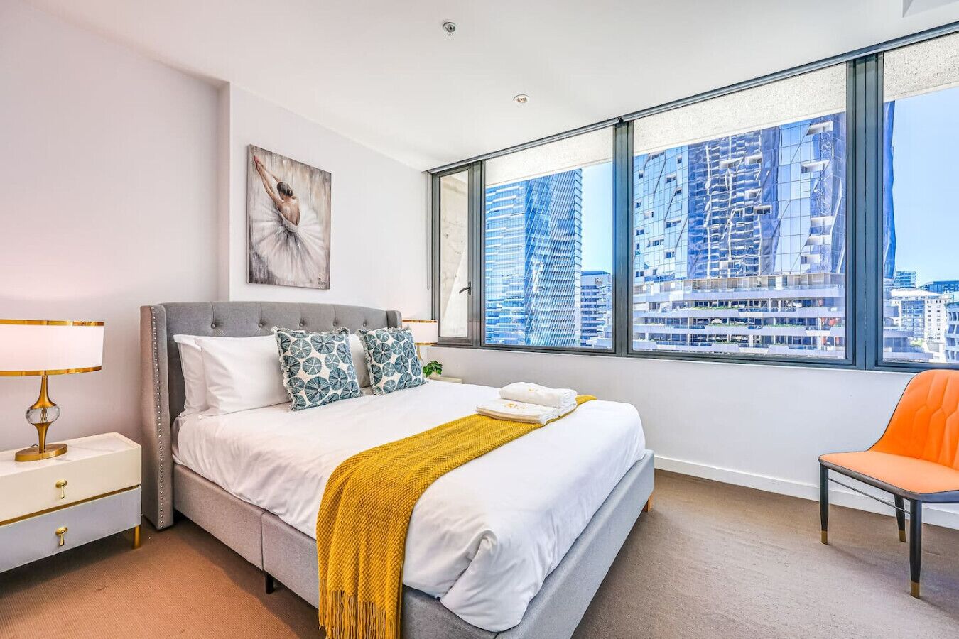 Een moderne hotelkamer met een groot bed, een nachtkastje, een stoel en uitzicht op de stad door grote ramen.