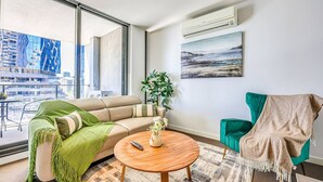 Una sala de estar moderna con un sofá, una mesa redonda de centro, un sillón verde, una planta y un cuadro en la pared.