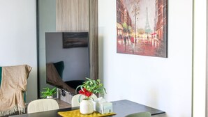 Una habitación moderna con una mesa de comedor, sillas, un florero con flores, un cuadro de una calle de la ciudad y un ventanal grande.