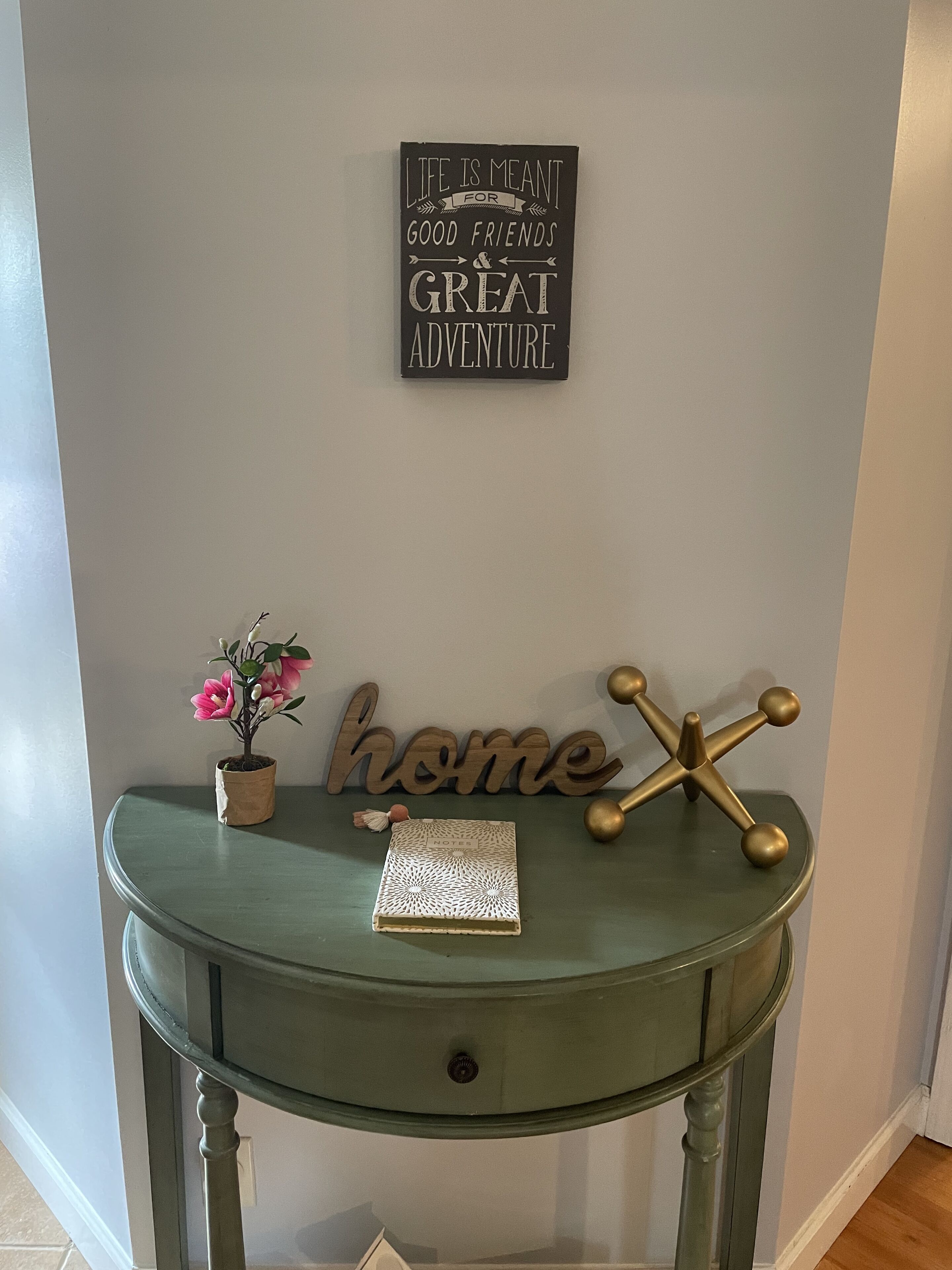 A green console table with a potted plant, a decorative item, and a sign on the wall.