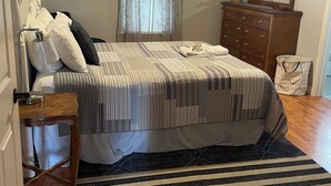 Une chambre à coucher comprenant un lit, une commode, un miroir, un ventilateur de plafond et une fenêtre avec des rideaux.