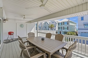 A covered outdoor deck with a table and chairs, a grill, and a view of colorful buildings.