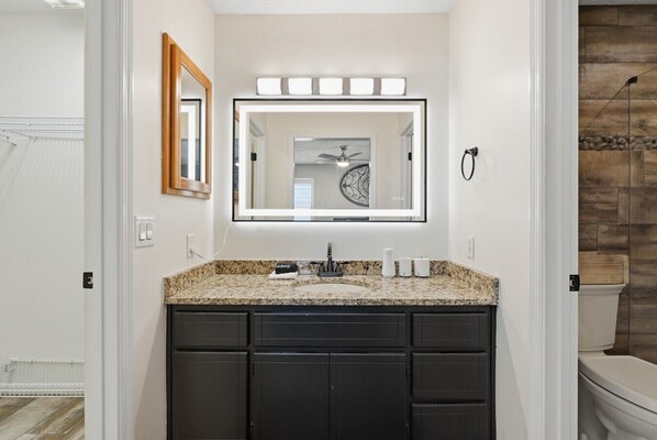 A bathroom with a granite countertop, black cabinets, a large mirror, and a wooden wall.