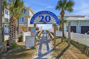 Un panneau indiquant l’accès à la plage, avec un palmier et un chemin menant à un bâtiment.