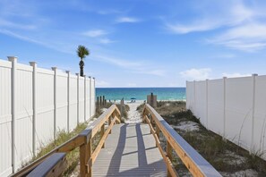 A wooden boardwalk leading to a beach with white fences on either side.