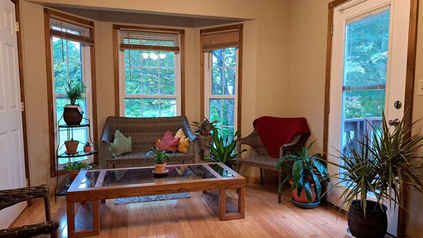 A cozy living room with a wooden floor, a glass coffee table, wicker furniture, and large windows with blinds. - Charming 3-bedroom house in peaceful Saint Francis, on the Bourbon Trail (Saint Francis)