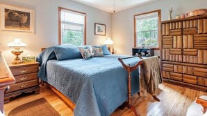 A bedroom with a bed, wooden dresser, two windows, a ceiling fan, and a nightstand with a lamp. - Charming 3-bedroom house in peaceful Saint Francis, on the Bourbon Trail (Saint Francis)