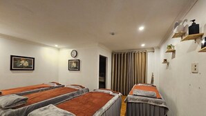 Een kamer met vier massagetafels, elk voorzien van een grijze deken en een oranje handdoek. Twee klokken hangen aan de muur, en er is een raam met gordijnen.