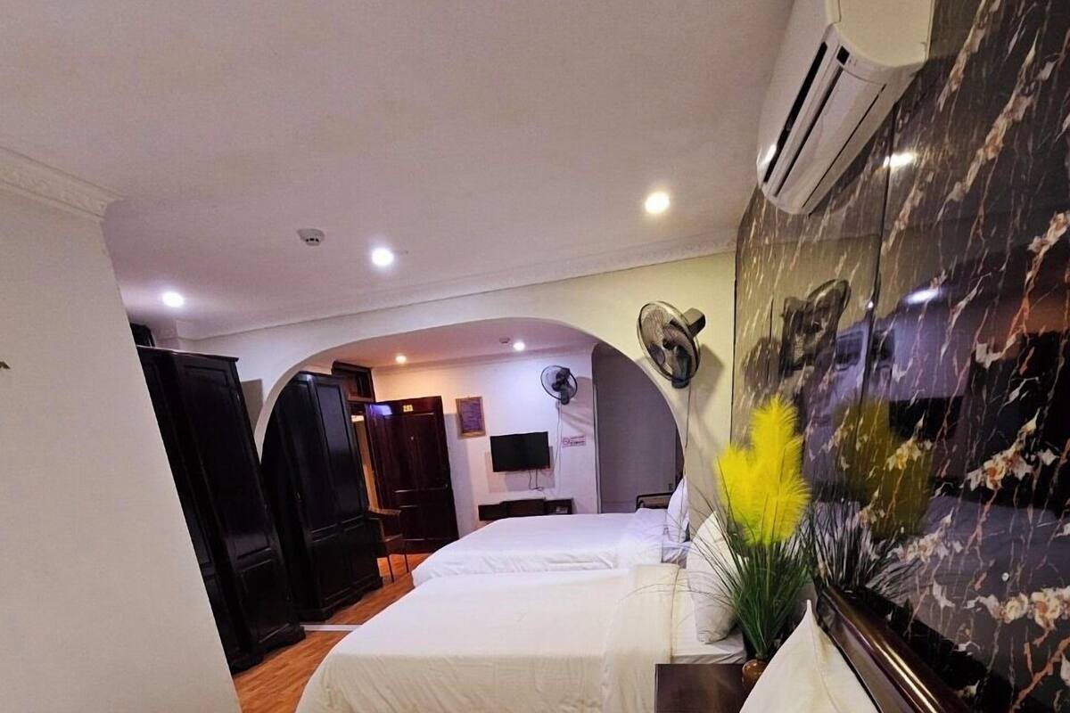 A hotel room with two beds, a TV, a fan, and a marble wall.