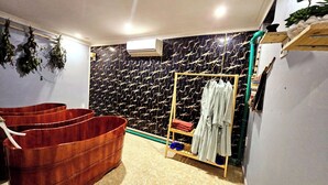 Een badkamer met een groot houten bad, een handdoekrek met badjassen en een marmeren wand.