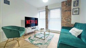 Un salón con un sofá azul verdoso, un sillón verde, una mesa de centro y un televisor que muestra el logotipo de Netflix.