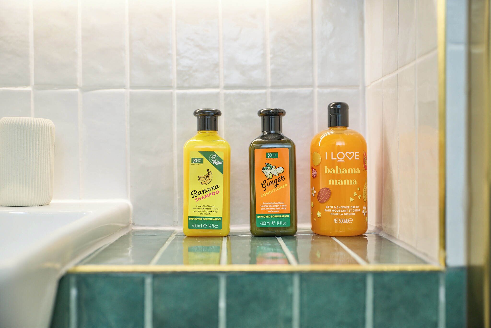 Three bottles of bath products on a tiled shelf.