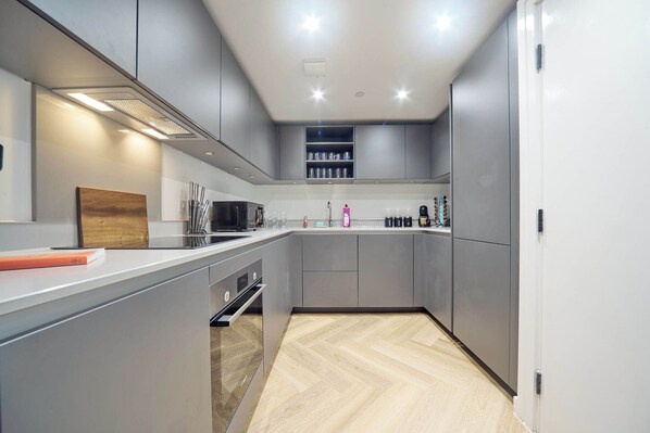 A modern kitchen with grey cabinets, a wooden countertop, and a built-in oven.