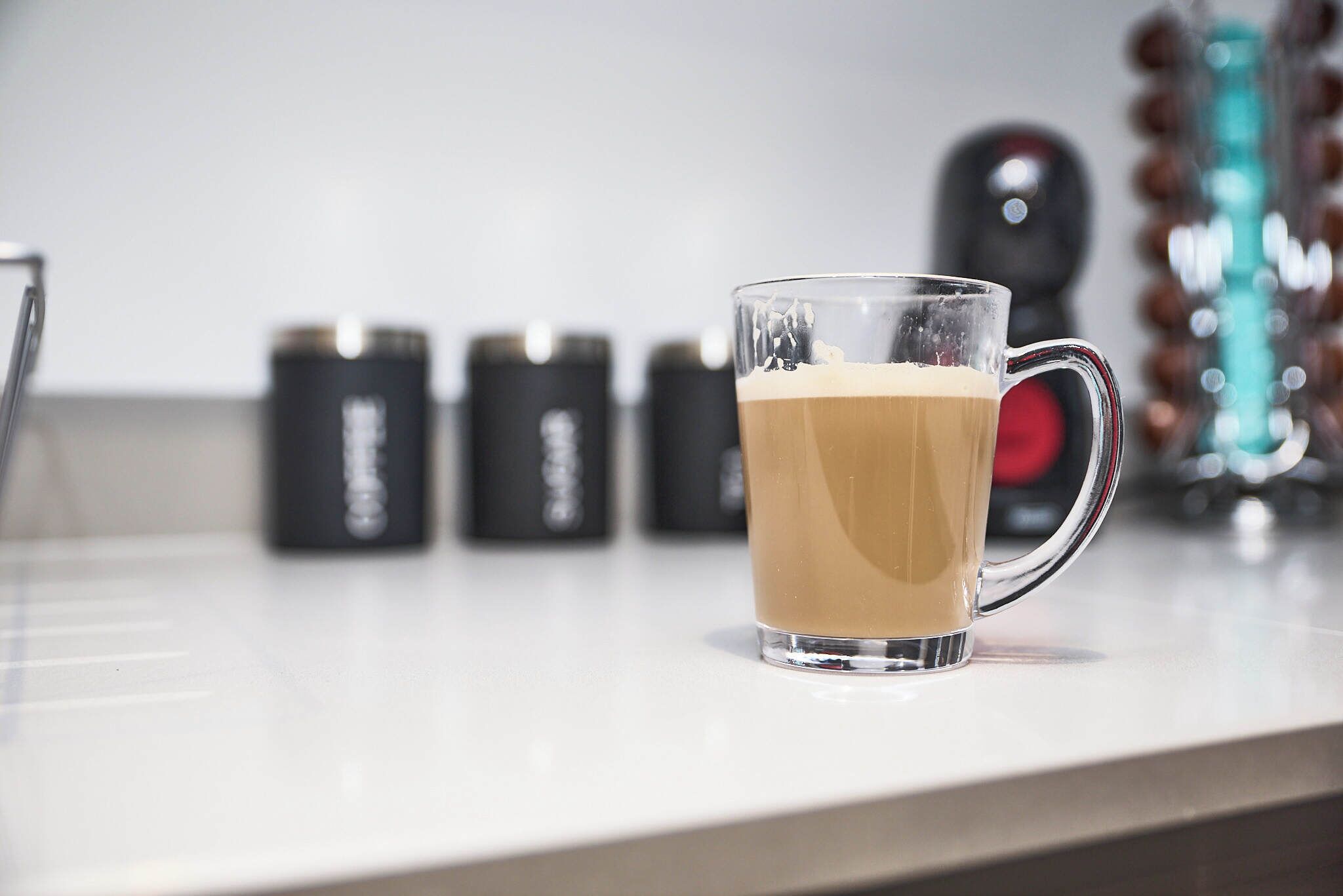 Una taza de vidrio transparente con asa sobre una encimera blanca.