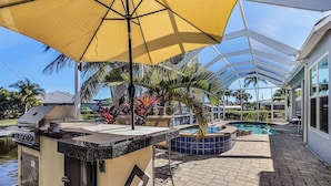 Un patio al aire libre con una parrilla, una piscina y un área cubierta con palmeras.