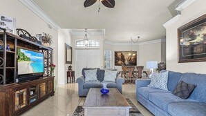 Una sala de estar con televisor, un sofá azul, una mesa de centro de madera y una araña.