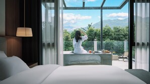 A modern hotel room with a large bed, a sitting area with a view of mountains and greenery, and a large window. - Z HOTEL - Qingchengshan (Chengdu)