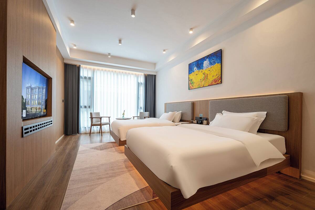 Habitación de hotel con dos camas, televisión, escritorio y un amplio ventanal con cortinas.