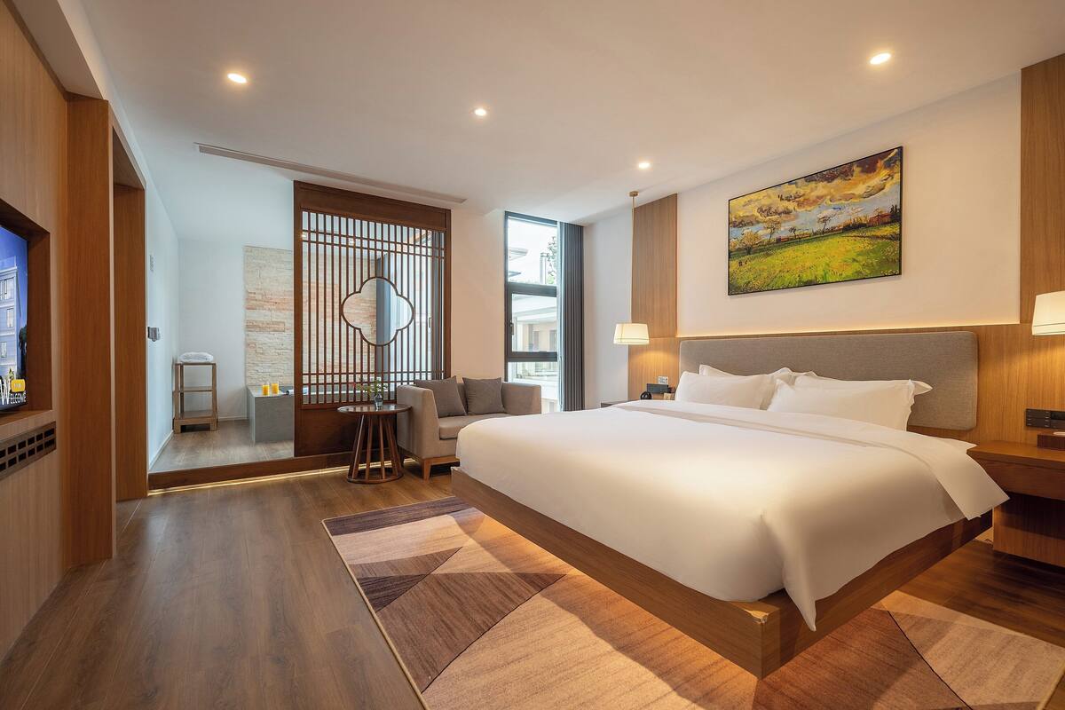 Una habitación de hotel moderna con una cama grande, un escritorio con silla, un televisor y un cuadro en la pared.