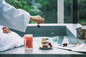 A person holding a cherry, a glass of red drink, and a layered dessert on a tray, with a pool and greenery in the background. - Z HOTEL - Qingchengshan (Chengdu)