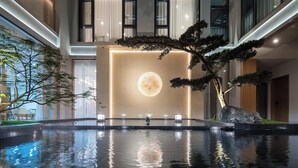 A modern indoor pool area with a reflective water surface, a large rock centerpiece, and a minimalist design. - Z HOTEL - Qingchengshan (Chengdu)
