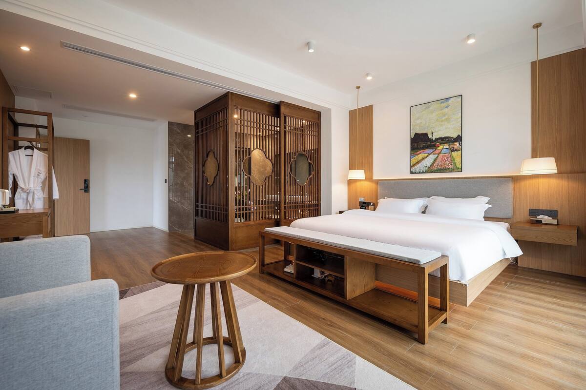 Una habitación de hotel moderna con una cama grande, un armario de madera, un escritorio con una silla y un cuadro en la pared.