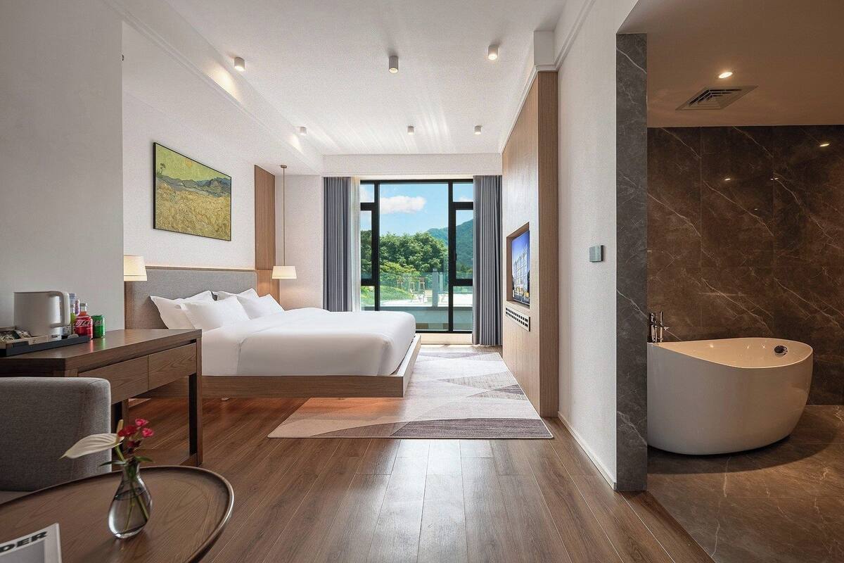 Una habitación de hotel moderna con una cama grande, un baño con bañera independiente y vistas a zonas verdes.