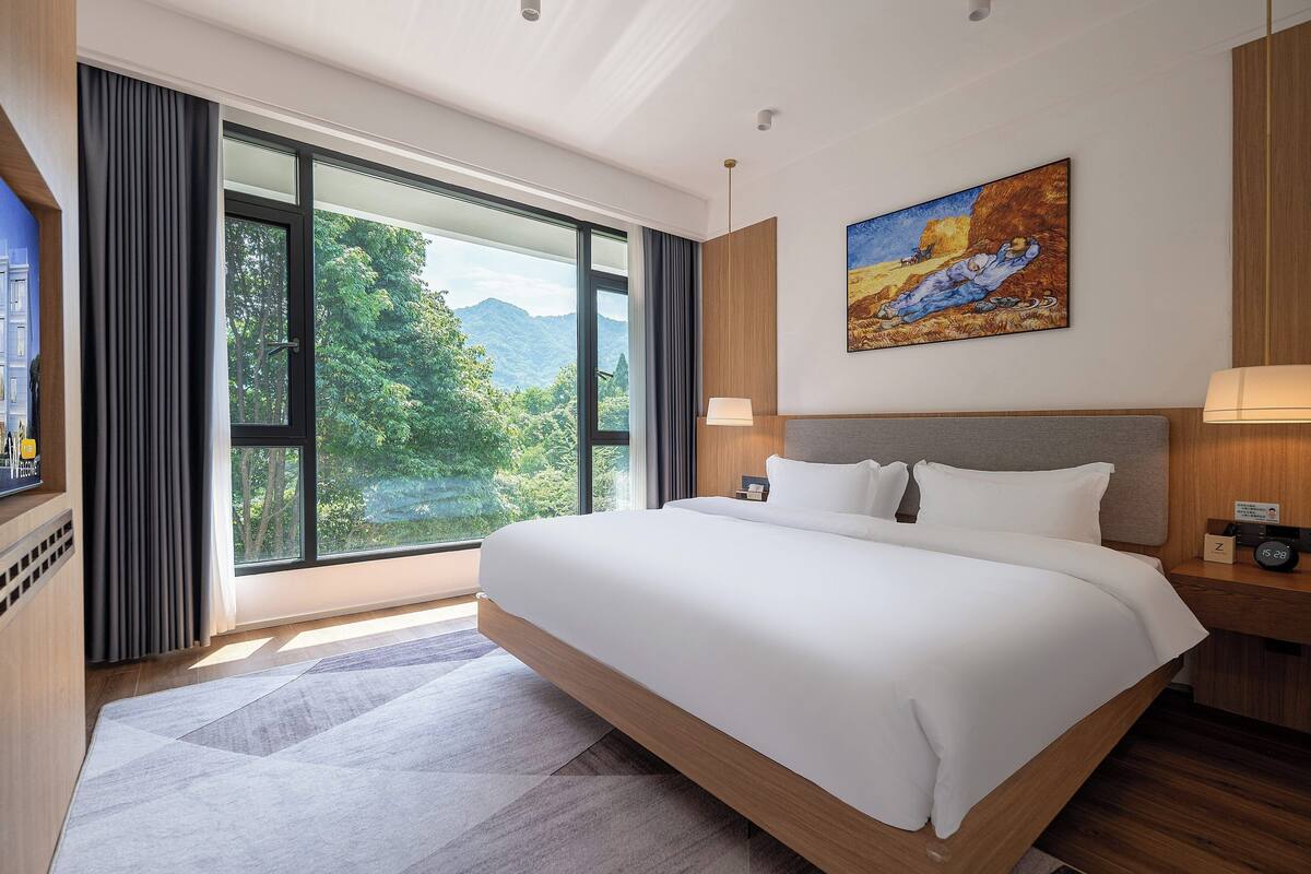 Habitación de hotel moderna con una cama grande, un cuadro y vistas a un paisaje montañoso.