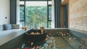 A room with a large window, a sofa, a small table, and a hot tub filled with rose petals. - Z HOTEL - Qingchengshan (Chengdu)