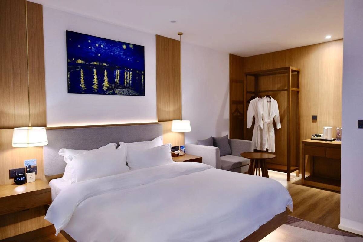 Habitación de hotel con una cama grande, un cuadro de cielo nocturno, una bata colgada y una mesita con una lámpara.