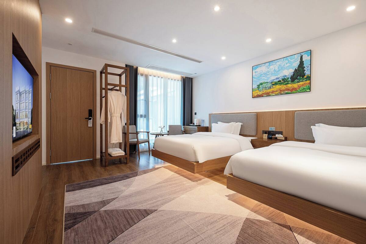 Una habitación de hotel con dos camas, un televisor, un cuadro y un armario de madera.