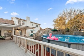 A backyard with a swimming pool, deck, and a house.