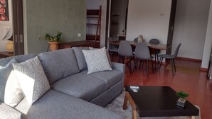 A modern living room with a grey sectional sofa, a black coffee table, and a dining area with grey chairs.