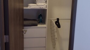 A hotel room with a walk-in closet containing folded towels, a water bottle, and a hanging rack.